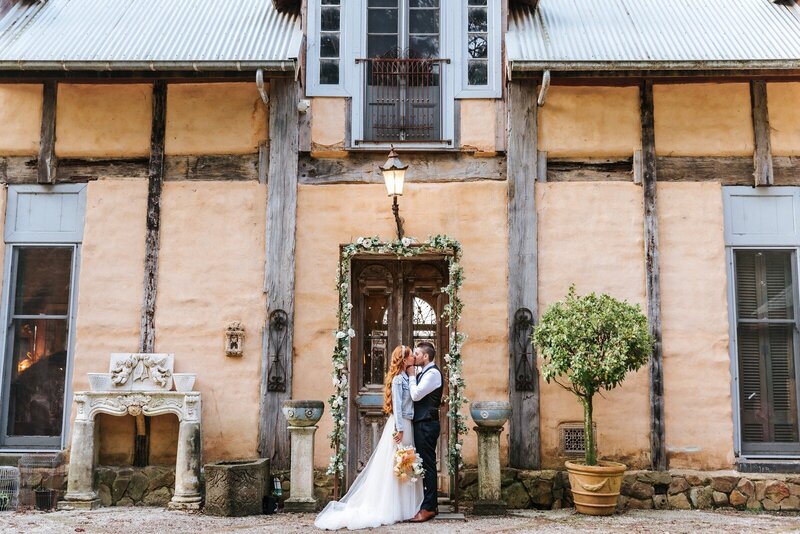 A couple kissing in front of the tuscan-inspired house at Mont Du Soleil Victoria.