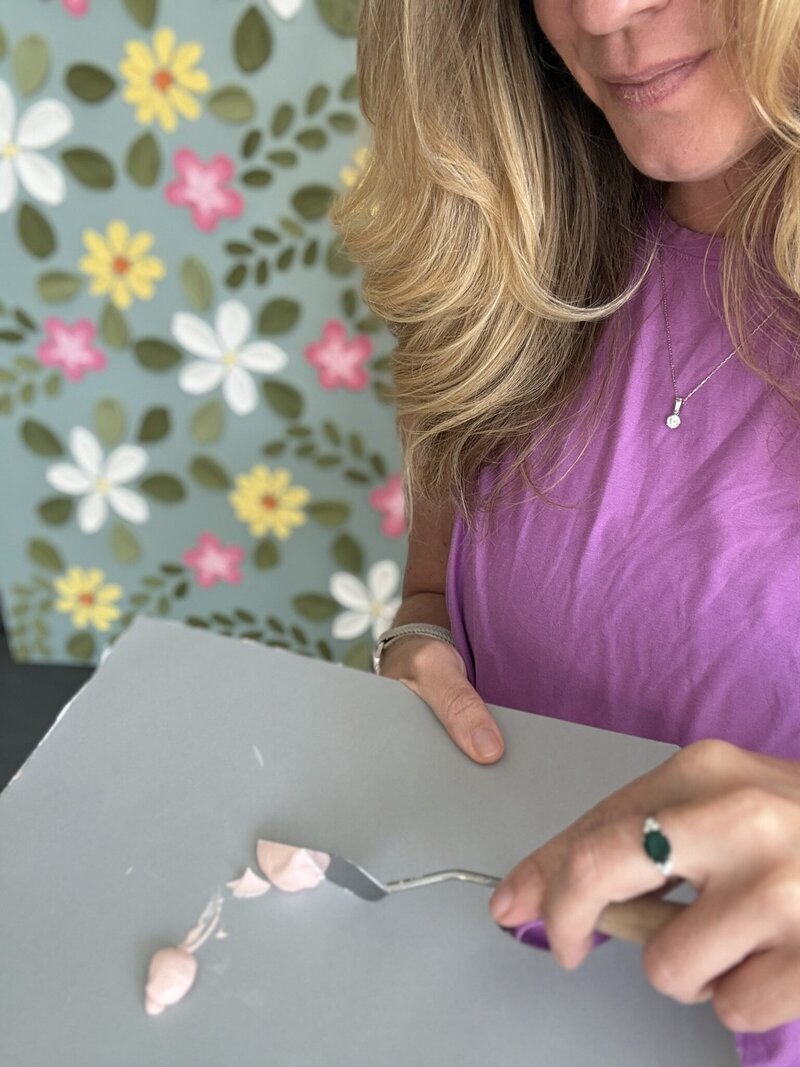 Palette knife pressing a raised pink petal into light modeling paste on canvas