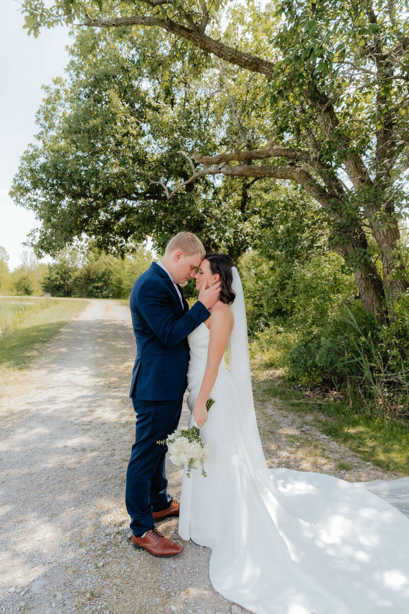 Bride and groom share quiet moment under tree-lined path, emotional Midwest wedding photography for romantic, connection-filled couples