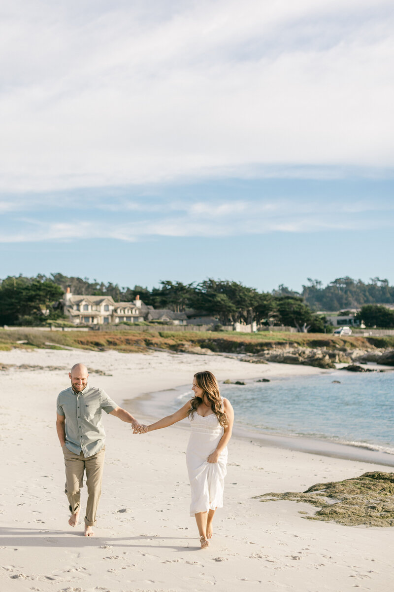 Playful Big Sur engagement session featuring a laughing bride-to-be on her partner’s back as they run through the water — captured with fashion-forward styling, candid movement, and editorial energy on the California coast.