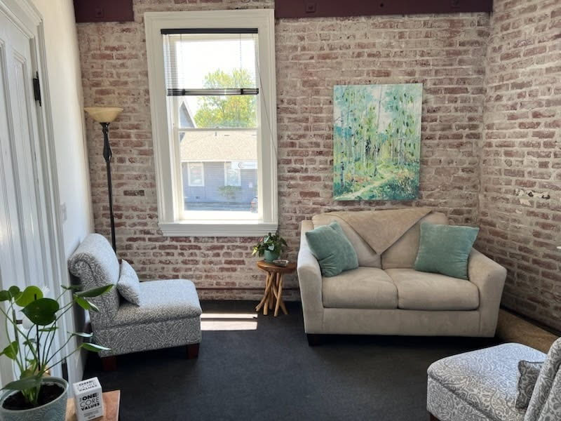 Warm therapy office with exposed brick, natural light, and comfortable seating for client sessions