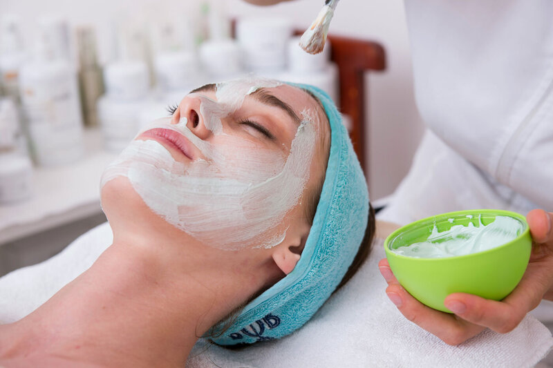 Esthetician applying a soothing hydration facial mask for dry skin at a Monroe, CT beauty salon.