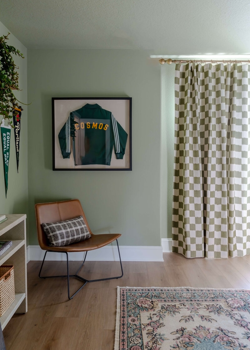 An example of maximalist interior design, featuring a framed sports jacket on the wall, checkered curtains and a leather chair in the corner. 