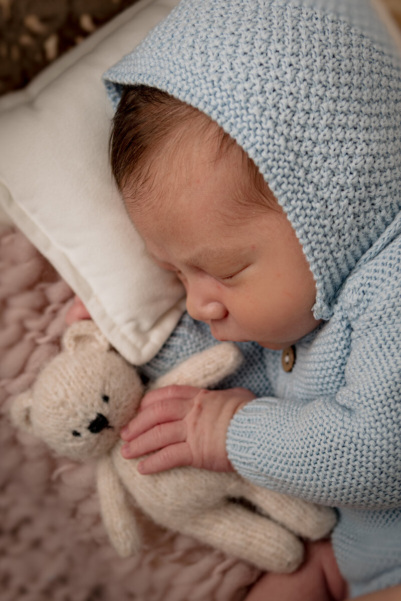 newborn baby boy wearing blue knit outfit snuggling with teddy bear