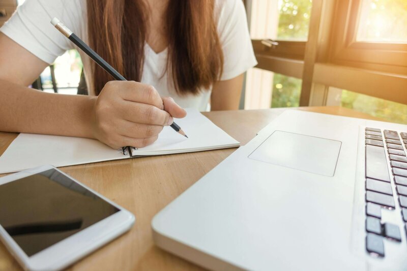 Woman writing in notebook with computer in front of her