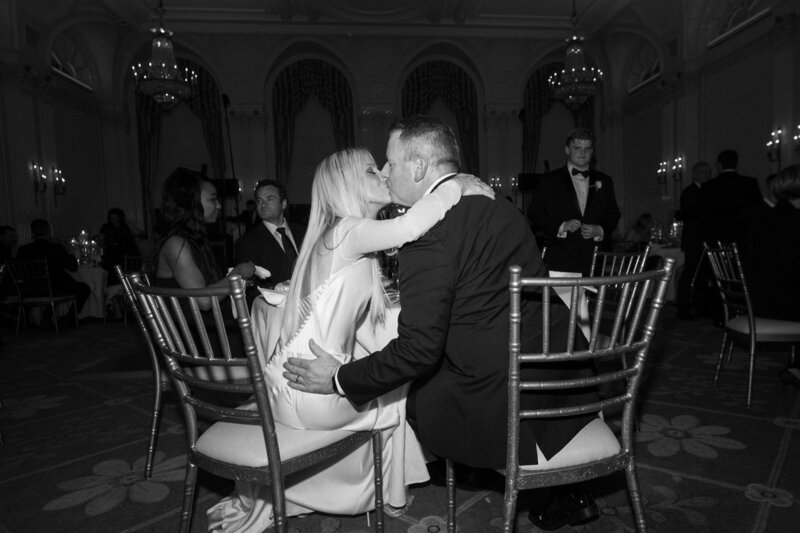 a bride and groom embrace under a large arch in black and white