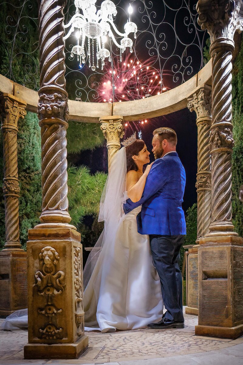 Bride and groom embrace on their wedding night as fireworks go off in the background