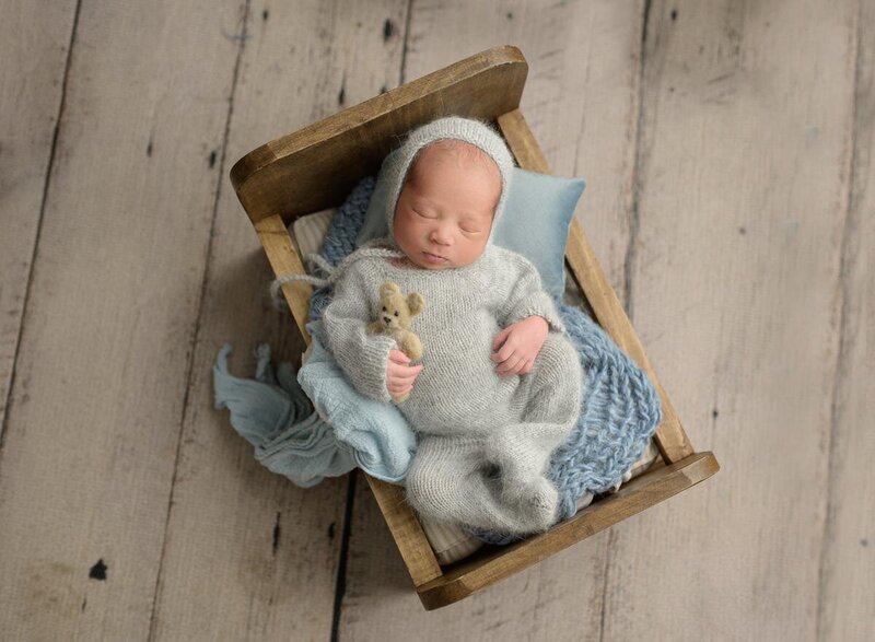 baby wearing a knitted sleeper and holding a tiny teddy bear