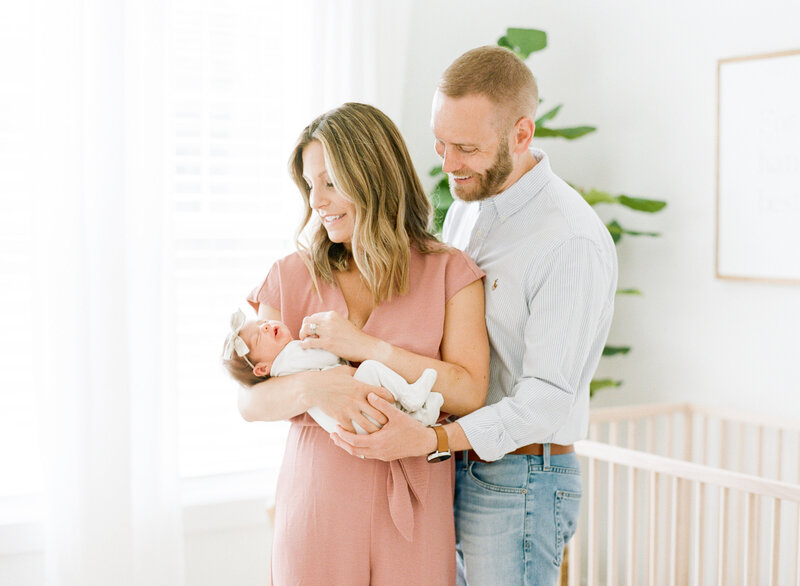 Mom and dad holding their new daughter in her nursery during their newborn session photographed in Raleigh NC. Photographed by Raleigh newborn photographers A.J. Dunlap Photography.