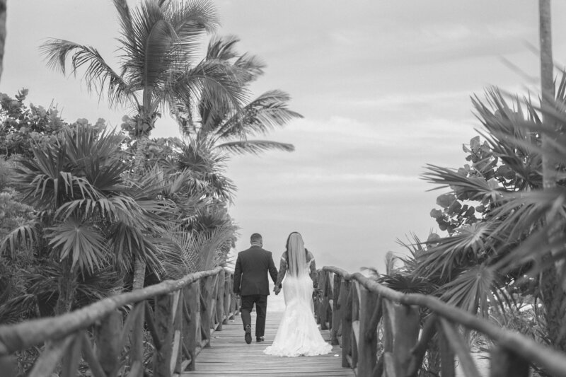 bride and groom holding hands while walking on the beach