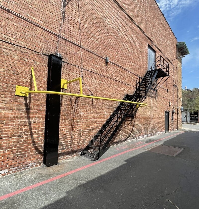 Black steel fire escape staircase with yellow safety rail installed on a commercial brick building exterior.