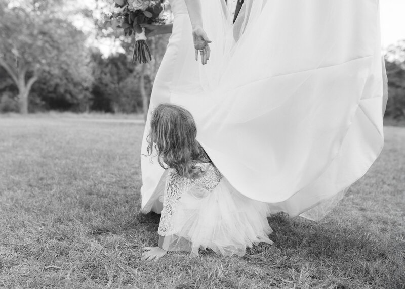 Black and white image of flower girl crawling under the train of bride's dress
