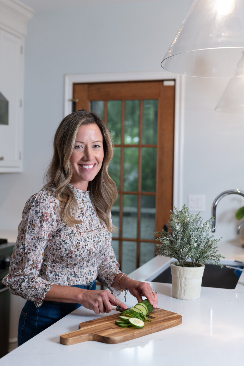 Jen, an integrative health coach, preparing a fresh cucumber in the kitchen, emphasizing her focus on healthy, wholesome meal preparation.