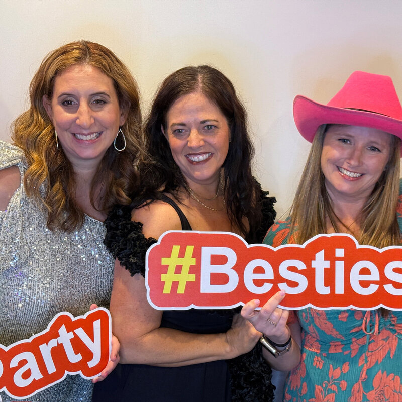 Three women holding “#Besties” party props