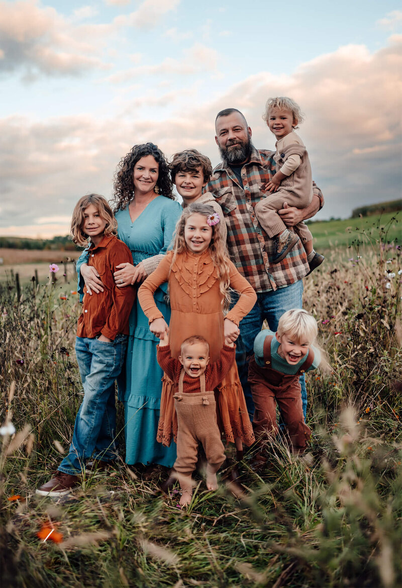 husband and wife with their 6 children posing in a weed field at sunset