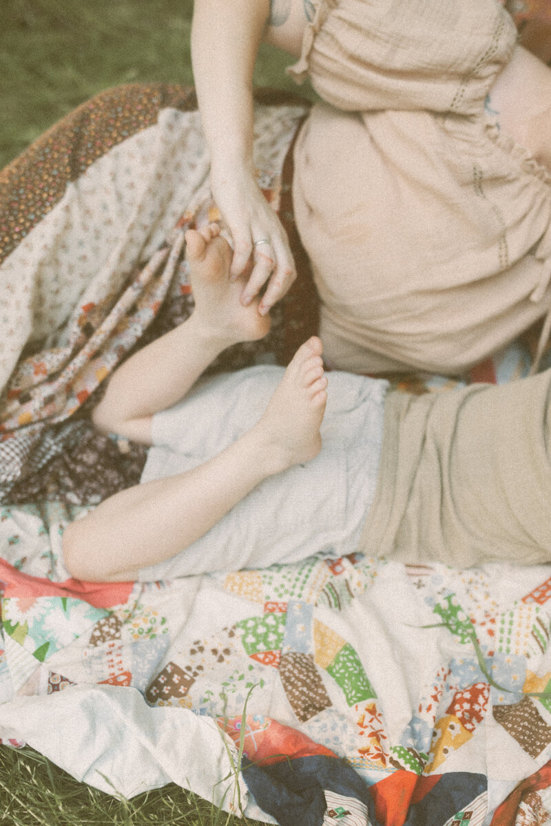 A mom tickling her sons bare feet while they are laying on a blanket. 
