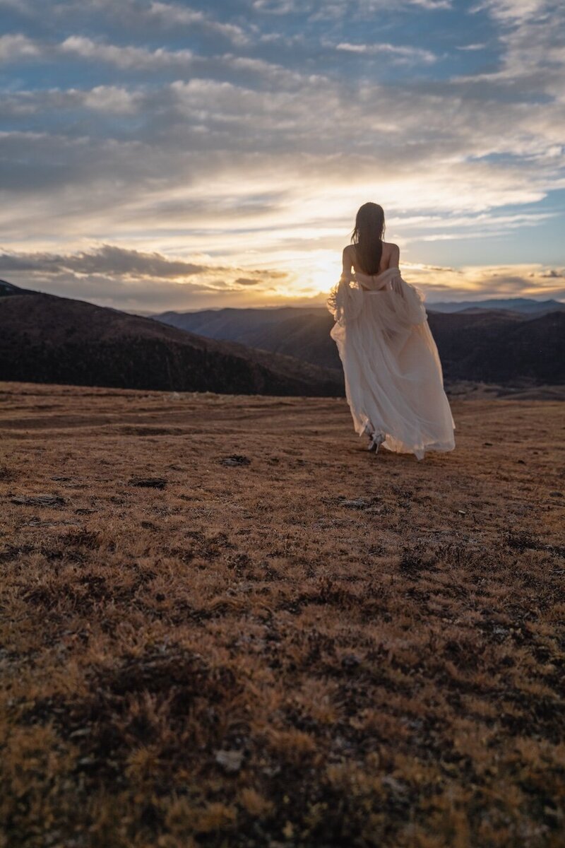 Couture dress bridal shoot on a field with mountains in the background and golden light.