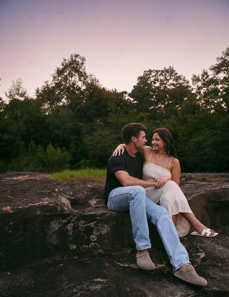 Couple sitting on a large rock formation lovingly smiling at each other.