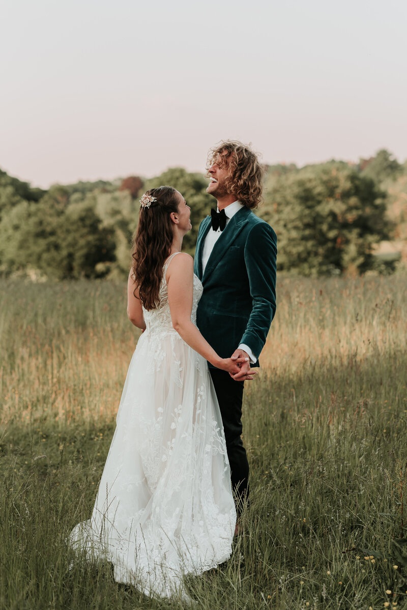 Beautiful bride and Groom in teal jacket laughing in the fields at Oak Tree Barn Weddings