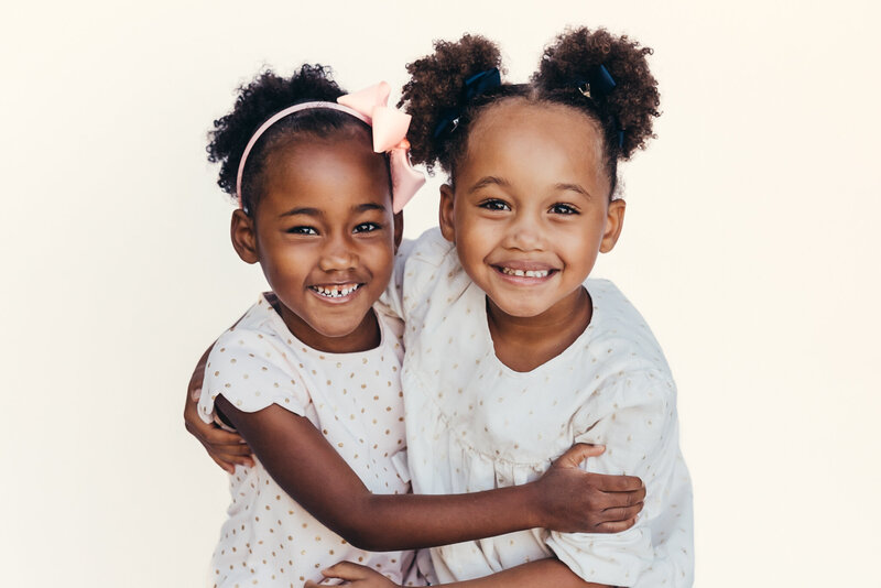 sisters hug together while having their portrait taken against a white backdrop