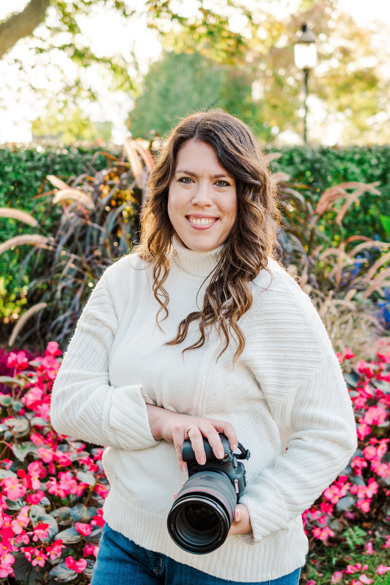 Meredith Mutza holding camera pink floral background in Frame Park, Waukesha Wisconsin.