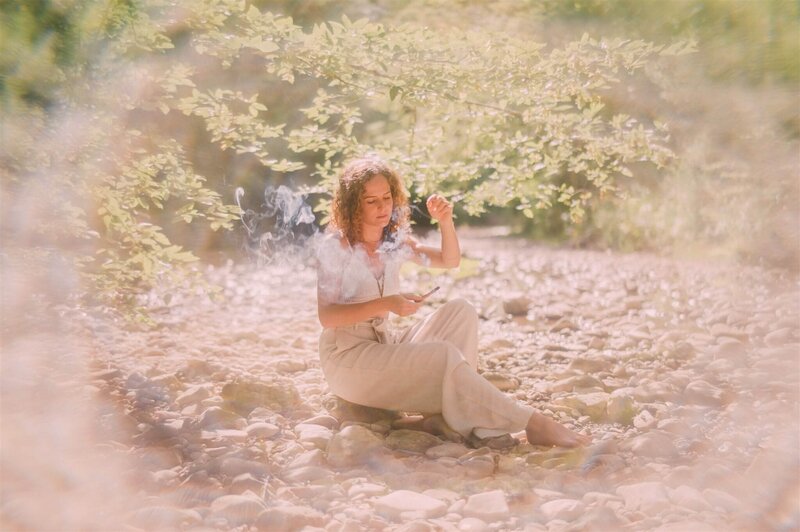 Frau sitzt mit Räucherstab auf einem Stein