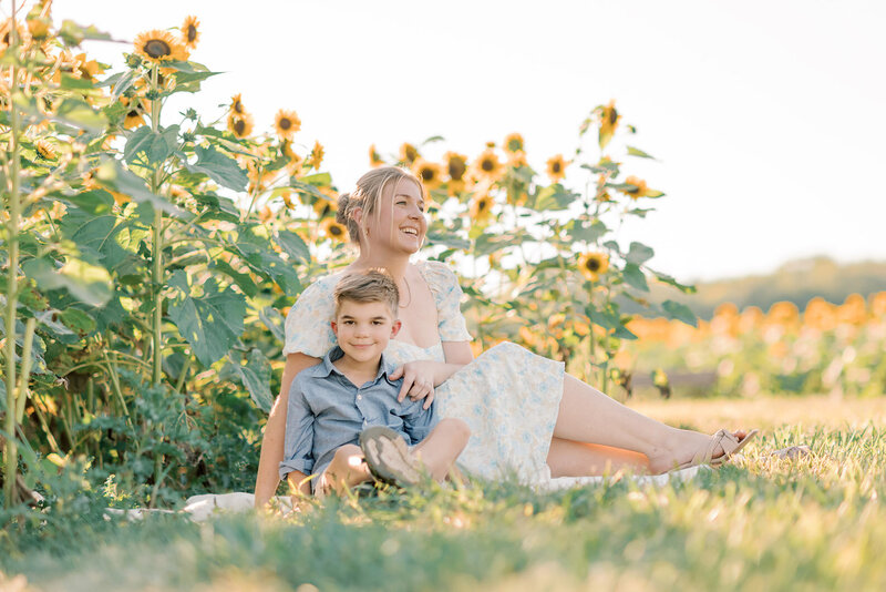 Mom in white dress and son in blue shirt in front of a sunflower field