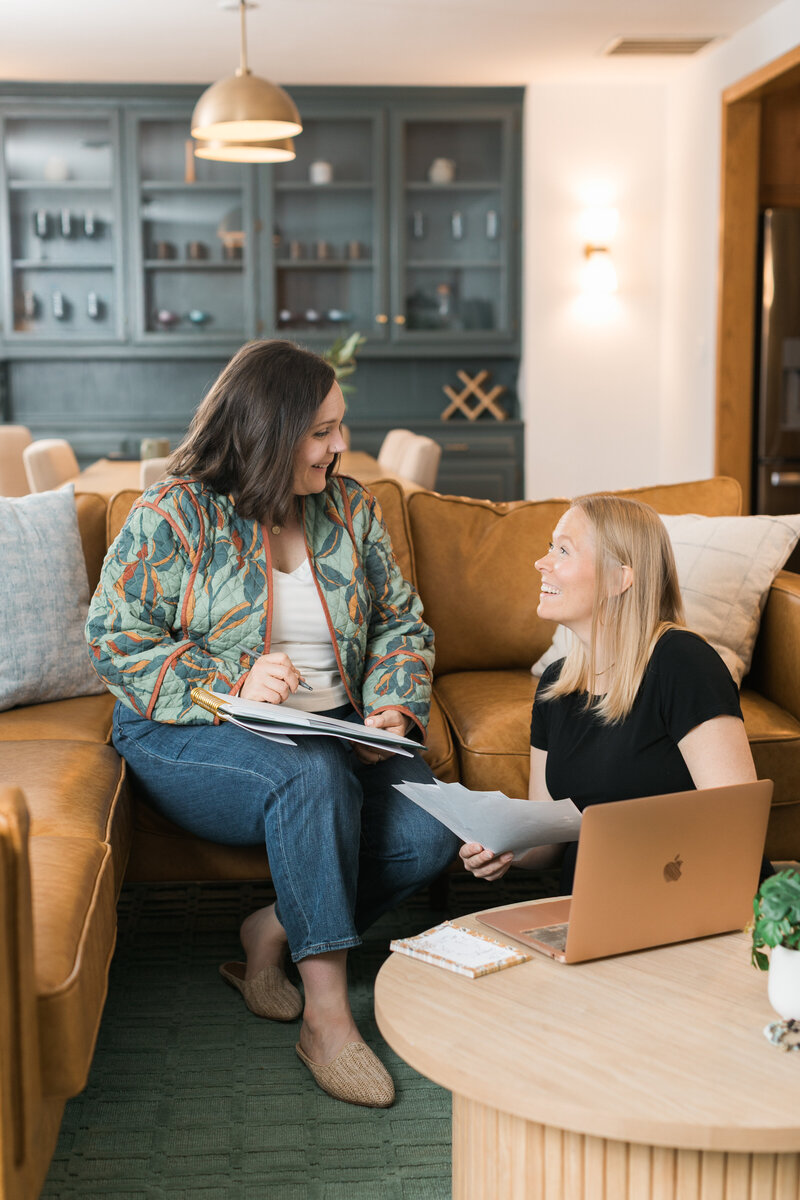 two women smiling while working at a laptop