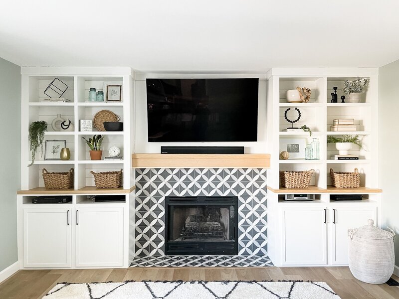 After photo of modern living room with white floor to ceiling cabinets and a playful tile on the fireplace.