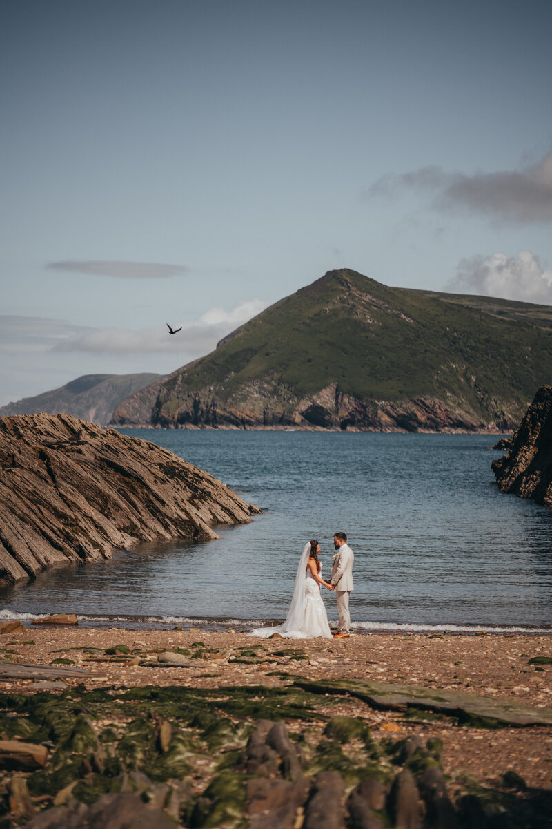 bride and groom stand at shoreline
