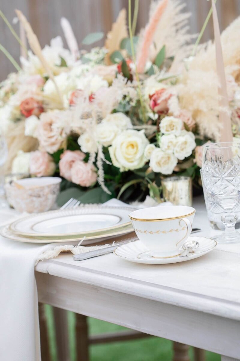 Afternoon tea table set up with tea cup, plates, cutlery and a beautiful white floral centrepiece