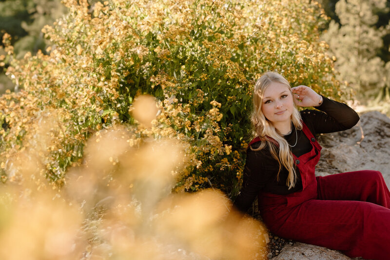 Senior girls sitting next to yellow flowers while playing with her hair