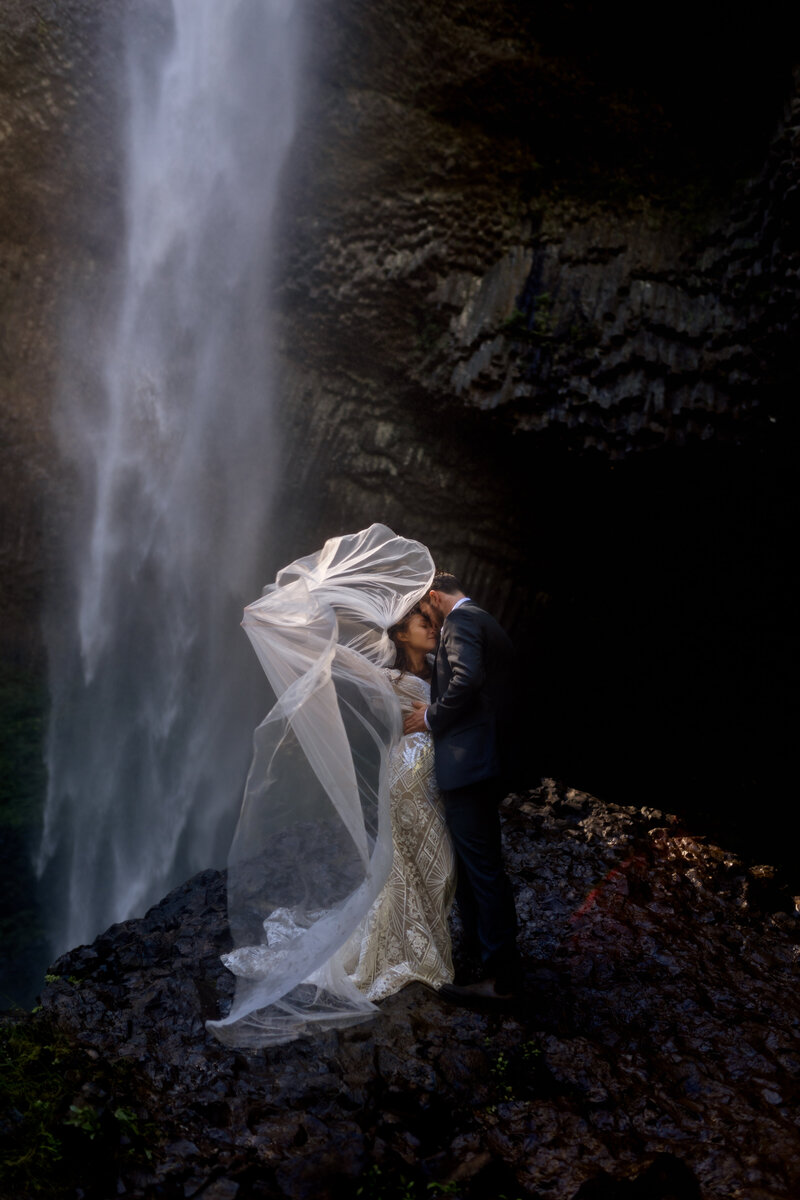 A stunning bridal portrait beneath a misty waterfall, creating an ethereal, adventurous vibe for Pacific Northwest photographers.