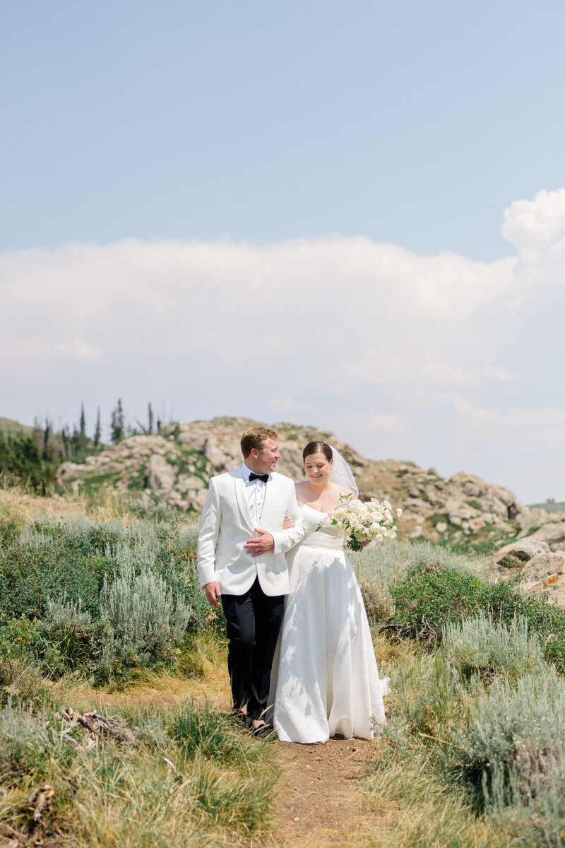 bride and groom walking arm in arm on top of the mountain