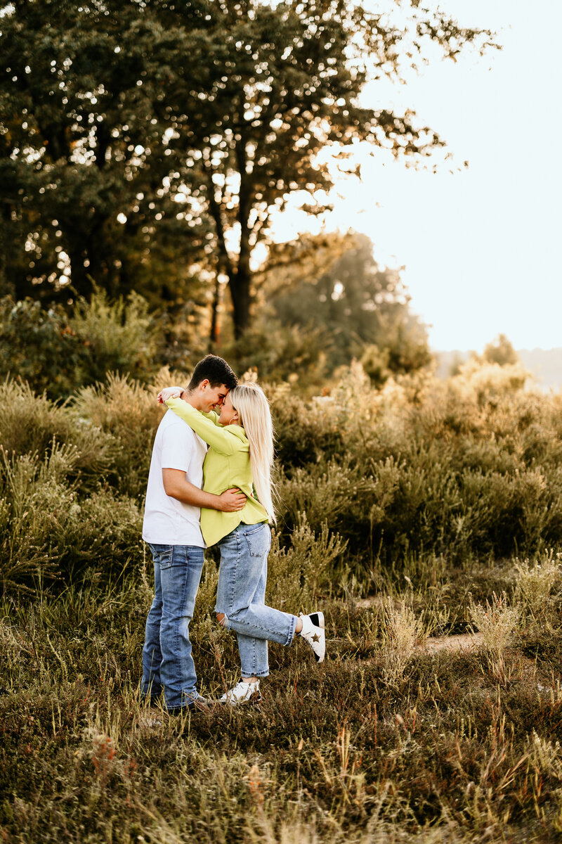 The engaged couple are facing each other, the bride to be has her arms draped around her fiancé's neck