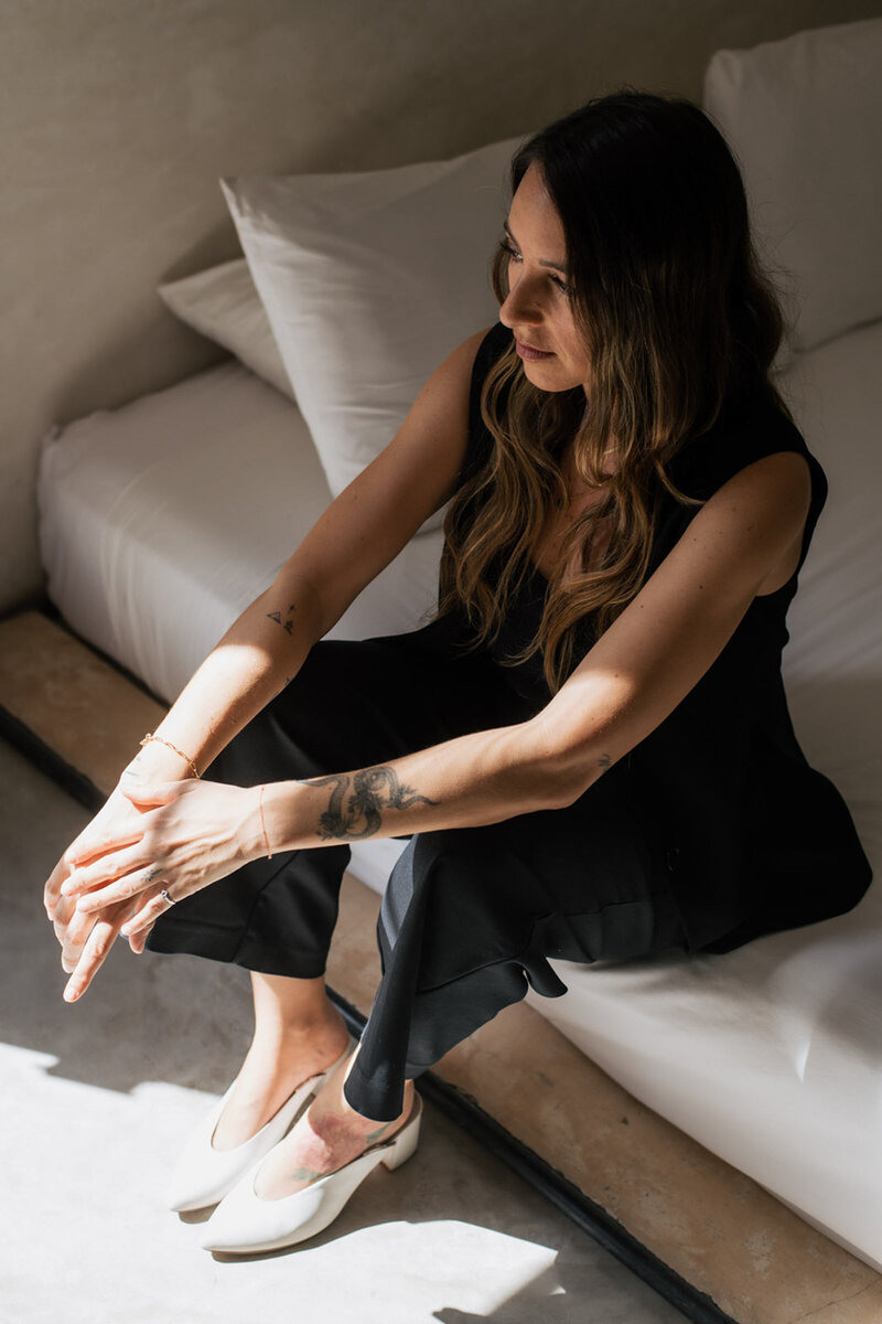 Cabo Photographer sitting with her arms gently overlapping across her knees wearing a black outfit.
