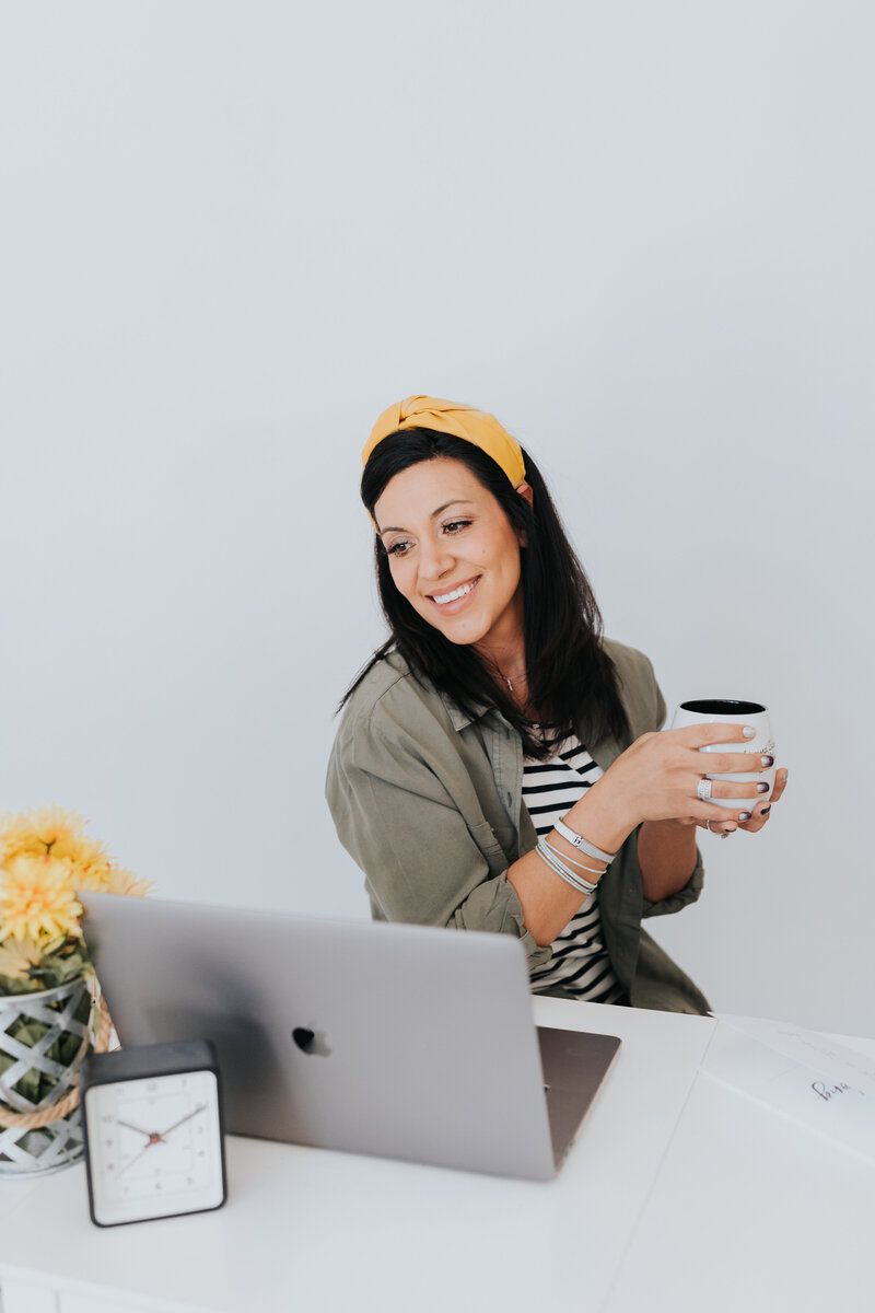 Christian woman with yellow headband  looks at computer and holds cup of coffee
