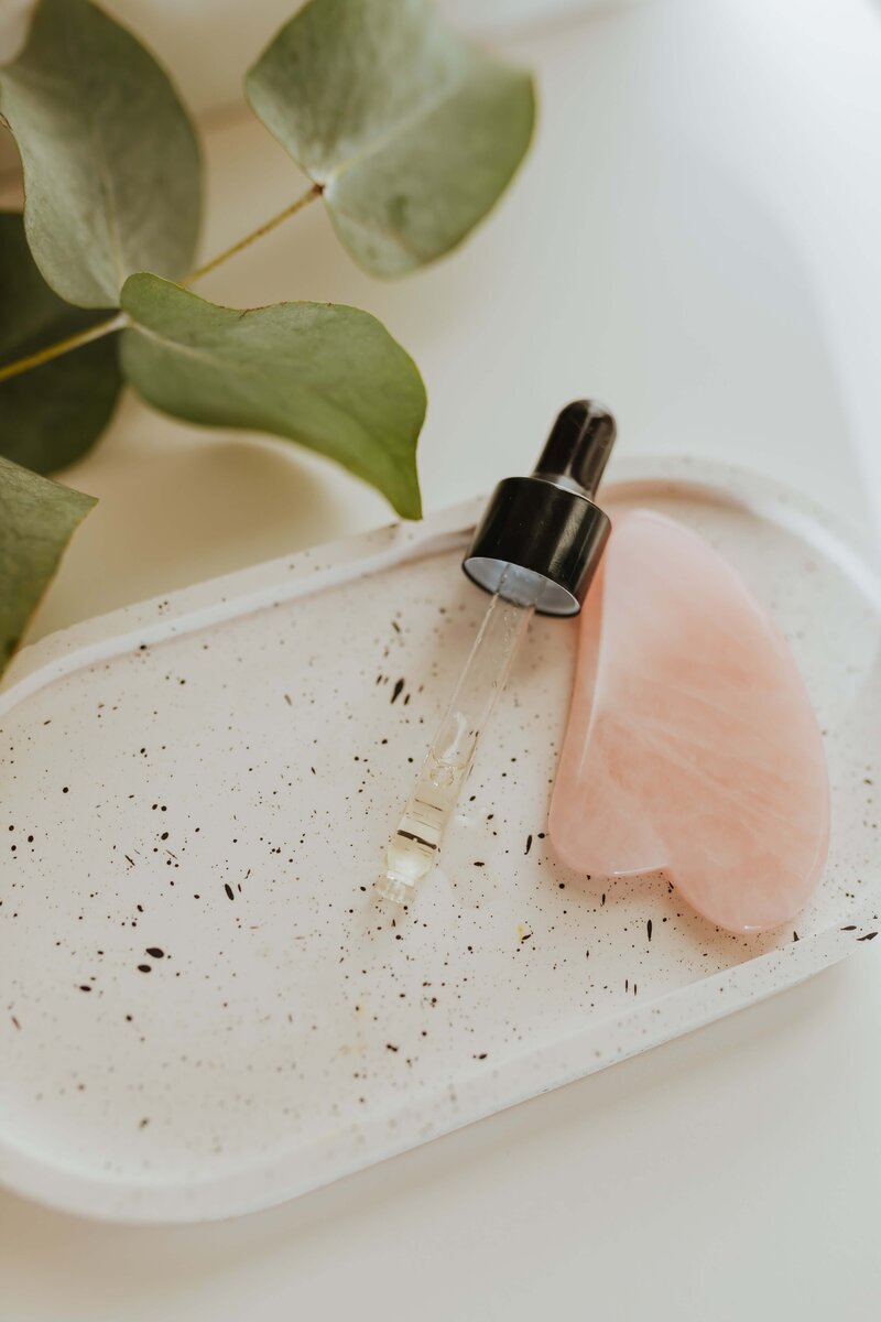 A skincare serum dropper and pink gua sha tool on a marble tray