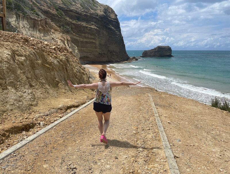 Young woman walking along a rocky path with ocean cliffs in the background
