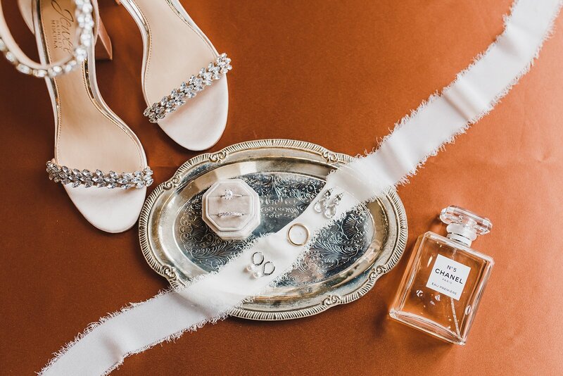 brides jewelry on a silver platter with her shoes and perfume bottle next to it