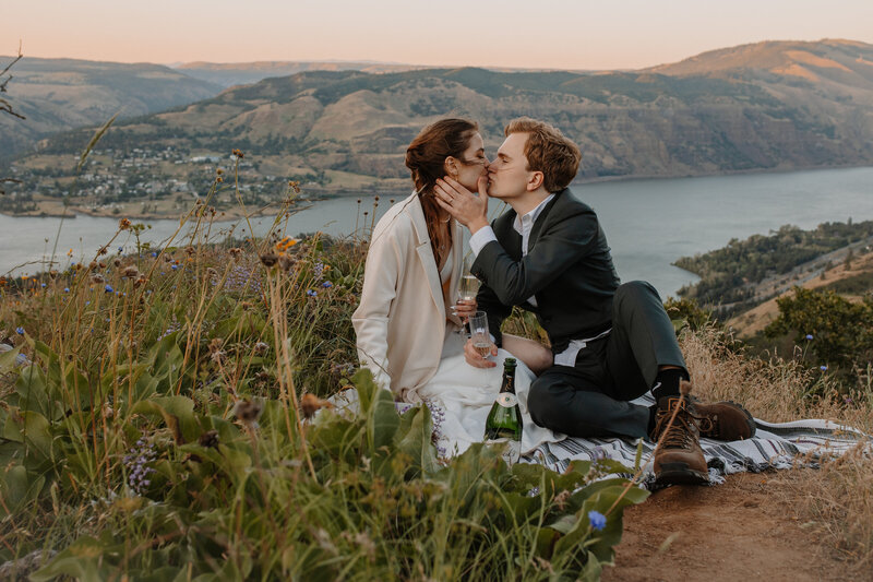 Bride and groom kissing on a picnic blanket overlooking river