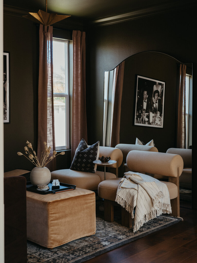 Moody modern living room with dark olive walls, velvet ottoman, sculptural accent chairs, and layered neutral textures by San Diego interior designer Natalie Barnas Interiors.