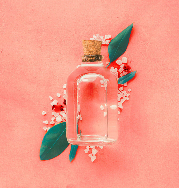 Flacon en verre et bouchon de liège  contenant un parfum émotionnel aux huiles essentielles. Arrière plan corail avec des feuilles et des cristaux.