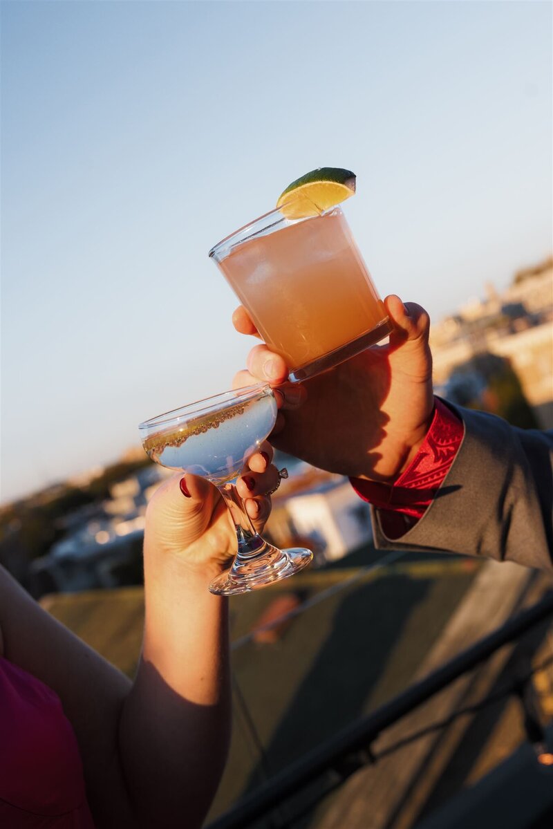 Couples hands holding signature cocktails cheersing on the terrace at the Line Hotel DC with the DC cityscape blurred in the background