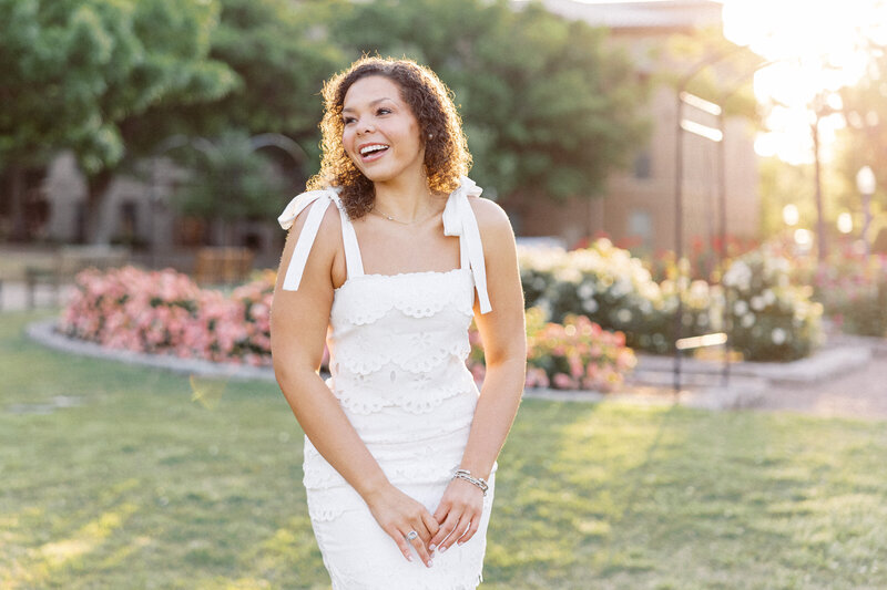 a curly haired OU senior laughs in the rose garden at the university of oklahoma campus for senior graduation photos - image by melanie foster photography