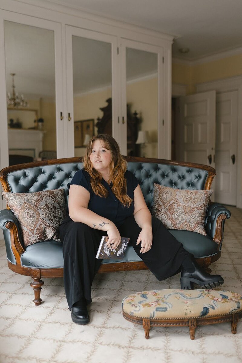 Woman sitting in an old building on a blue couch holding a book