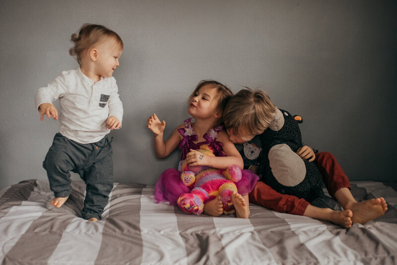 3 kids playing on a bed