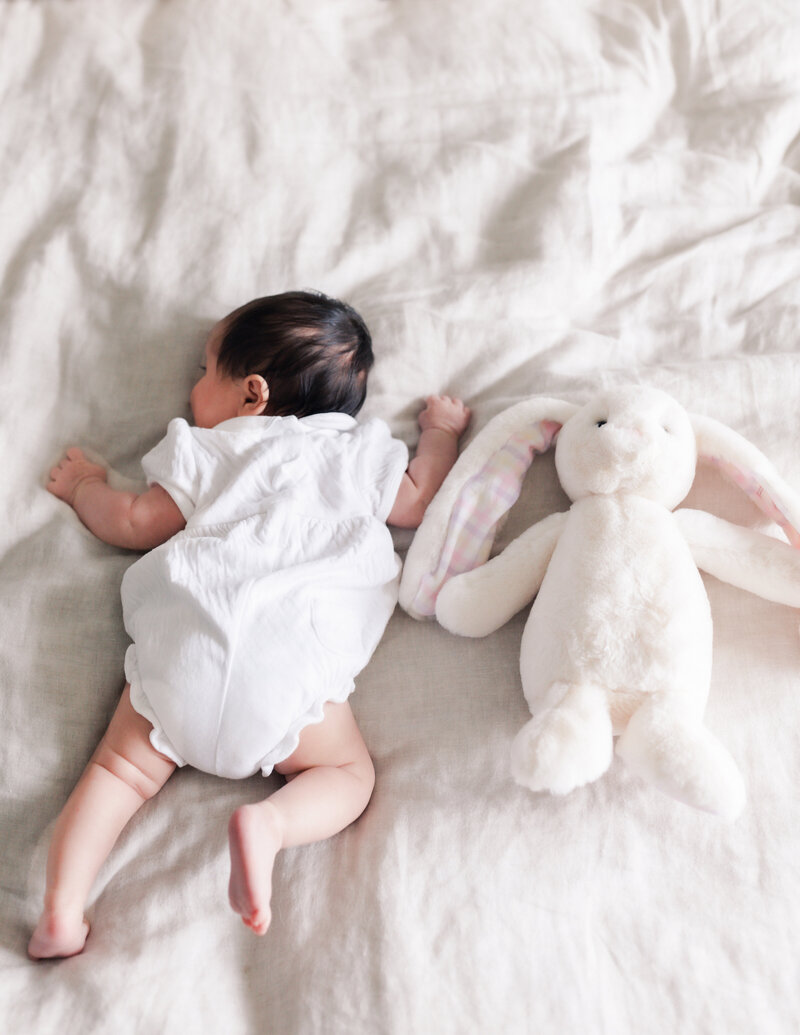 A newborn curls up near her bunny toy during a newborn session