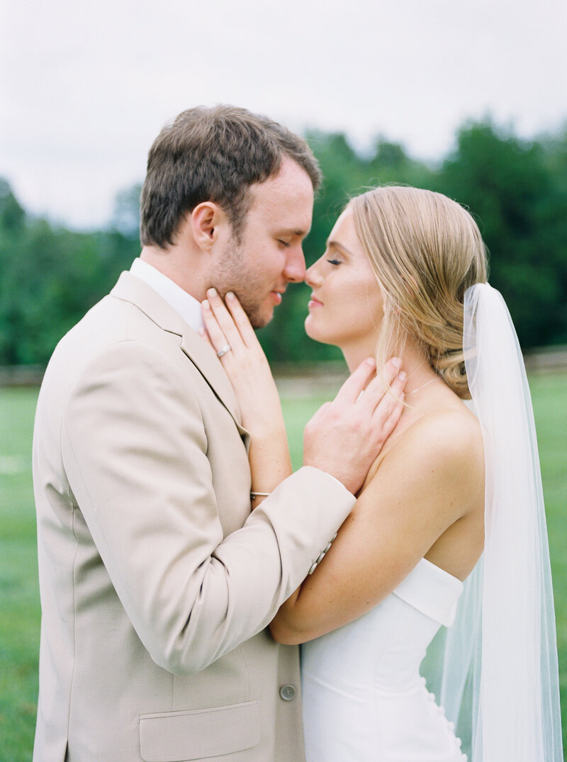 bride and groom touching each others faces while closing their eyes