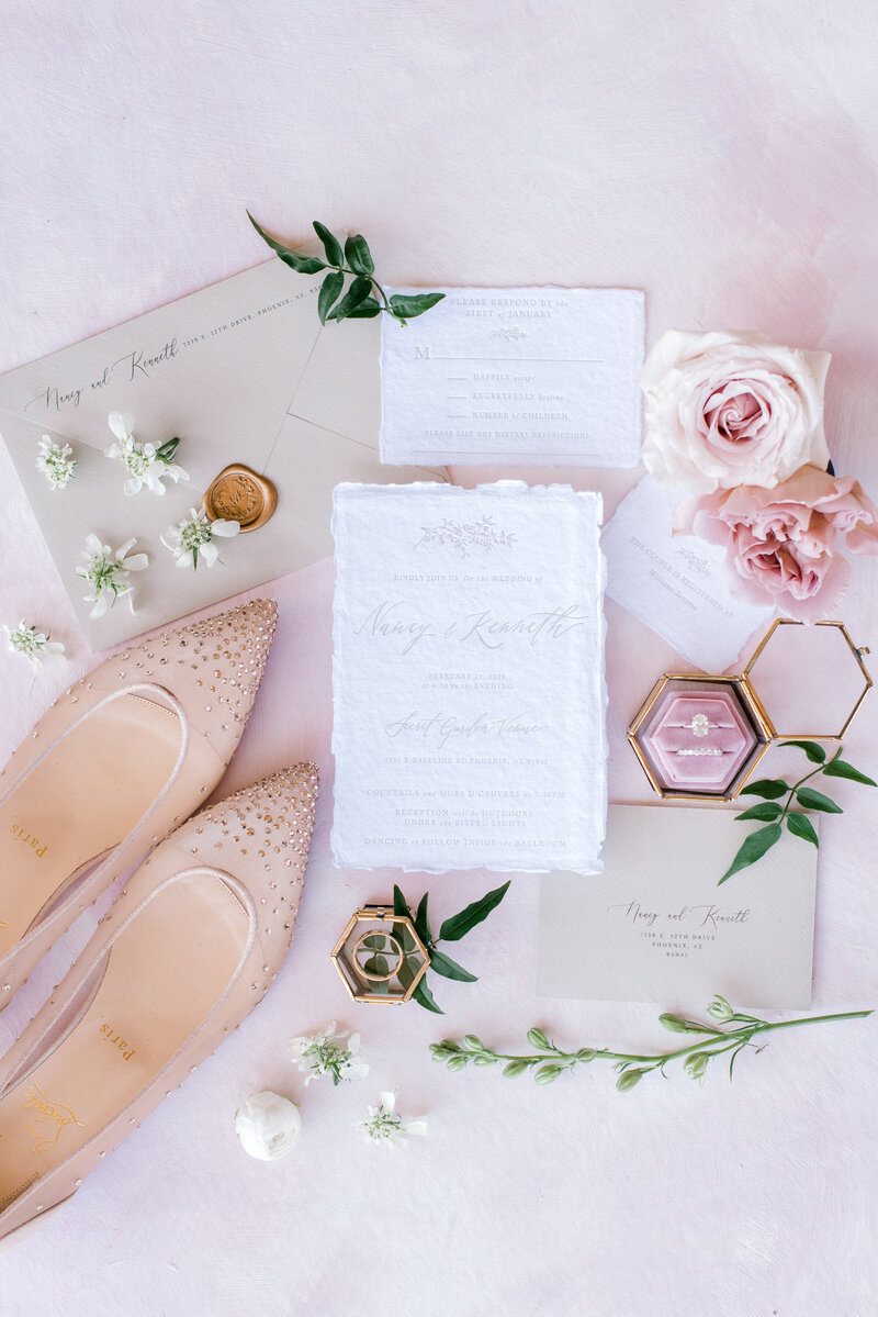Wedding flat lay with pink florals, shoes, and invitations
